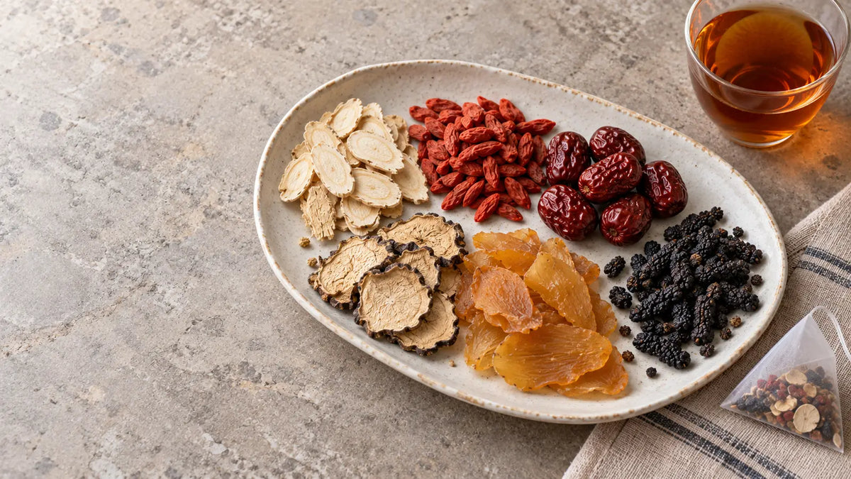 Dried ginseng five treasure tea herbs on a ceramic platter with a glass of amber herbal tea
